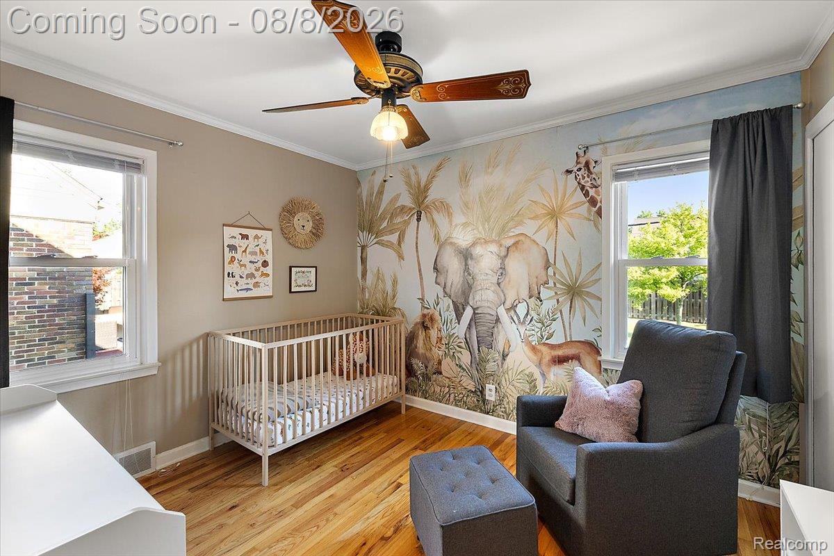 1150 West Eleven Mile Road Berkley, MI 48072 - Photo 13 of 29 Charming nursery featuring warm wood-finish flooring, a white modern crib, and a striking mural wall depicting wildlife and botanical elements