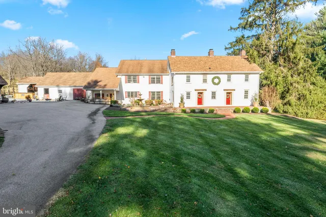 a view of a white house in front of a yard with plants and trees