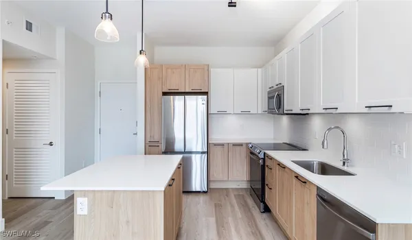 a kitchen with stainless steel appliances a refrigerator a sink dishwasher a stove and white cabinets with wooden floor