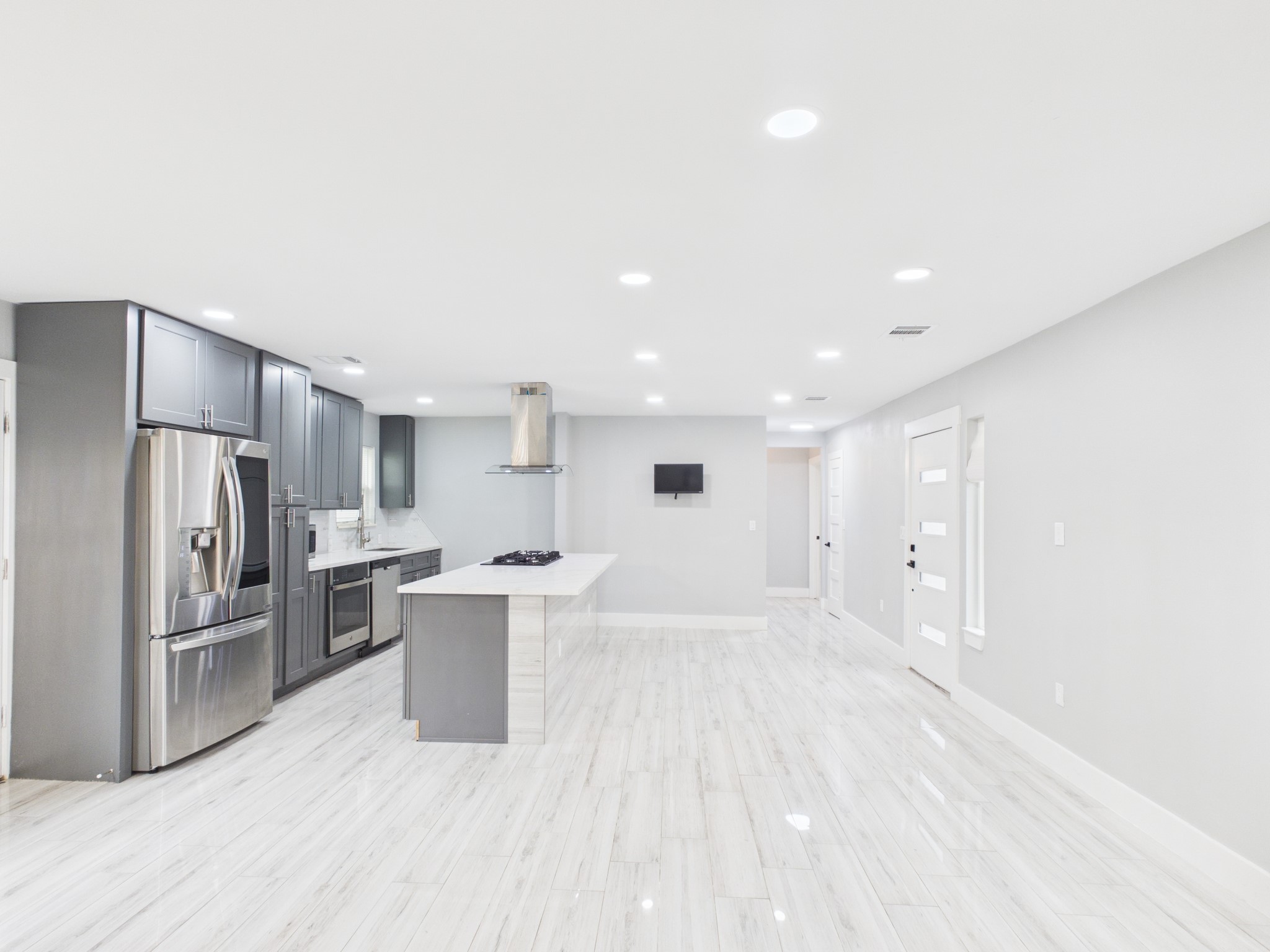 4927 Kelso Street Houston, TX 77021 - Photo 14 of 45 This photo showcases a modern, open-concept kitchen and living area with sleek gray cabinets, stainless steel appliances, and a large island. The space is bright and airy, featuring recessed lighting and light-colored flooring, creating a welcoming and contemporary atmosphere.