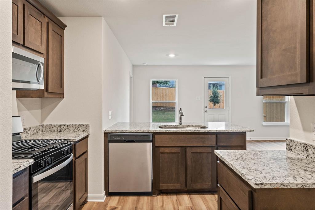 937 Burlington Avenue Fort Worth, TX 76108 - Photo 2 of 5 Kitchen featuring appliances with stainless steel finishes, light wood-style flooring, light stone countertops, dark brown cabinets, and a peninsula