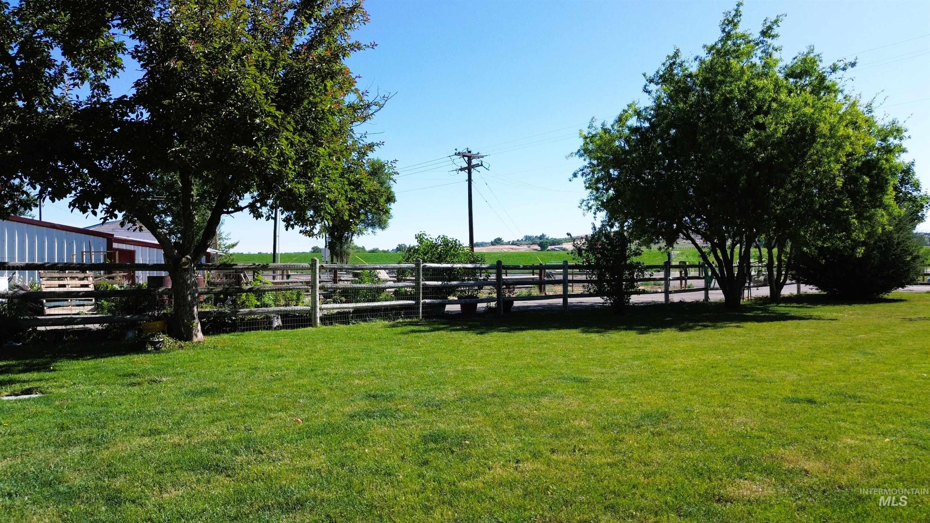 16985 Garnet Road Wilder, ID 83676 - Photo 36 of 39 Expansive grassy lawn bordered by a split-rail fence, mature trees, and distant agricultural fields