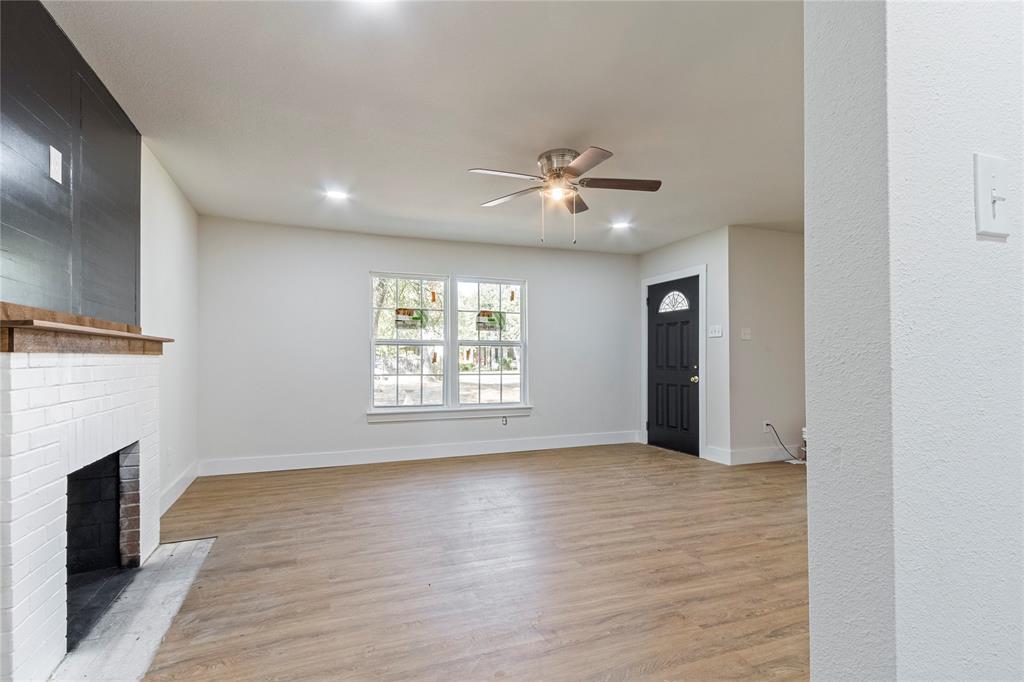 2029 Lynnhaven Road Fort Worth, TX 76103 - Photo 4 of 13 Wood-finish flooring with white baseboards, a white brick fireplace with a wood mantle, a ceiling fan with integrated lighting, recessed ceiling lights, and a dark entry door with decorative glass
