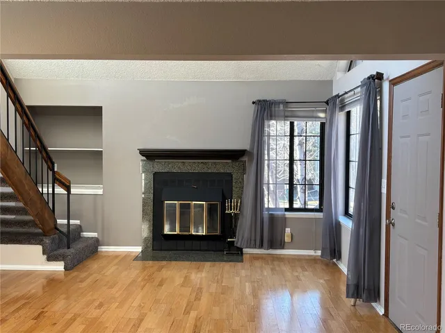 a view of an empty room with wooden floor fireplace and a window