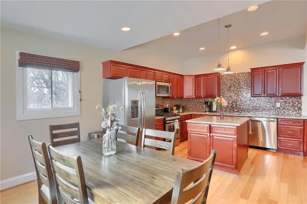 a kitchen with stainless steel appliances granite countertop a stove top oven a sink dishwasher a dining table and chairs with wooden floor