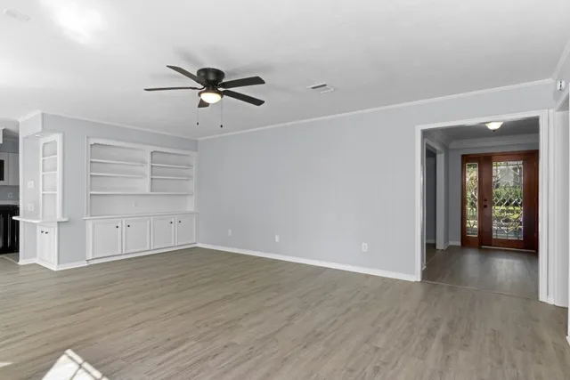 an empty room with wooden floor chandelier fan and windows