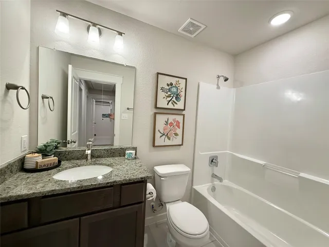 a bathroom with a granite countertop sink a toilet a mirror and bathtub