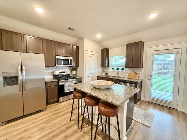 a kitchen with kitchen island granite countertop wooden floor cabinets and stainless steel appliances