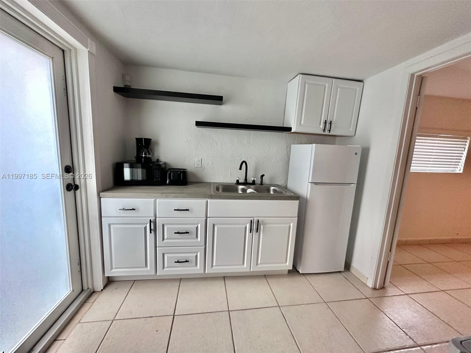 1375 Northwest 84th Terrace, Unit A Miami, FL 33147 - Photo 2 of 11 a kitchen with white cabinets a refrigerator and a sink