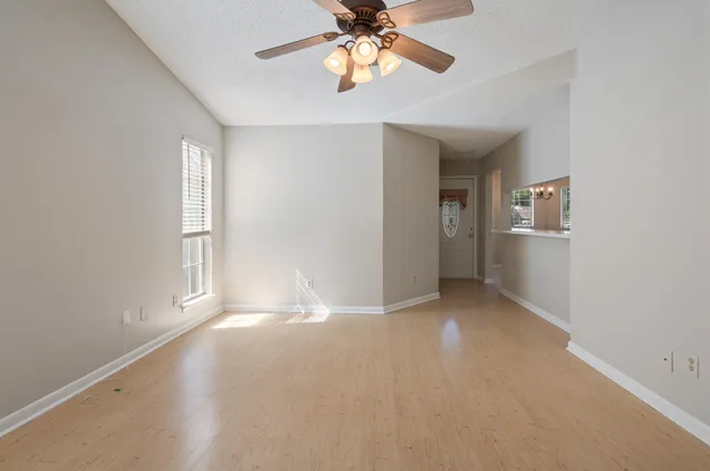 an empty room with chandelier fan and windows