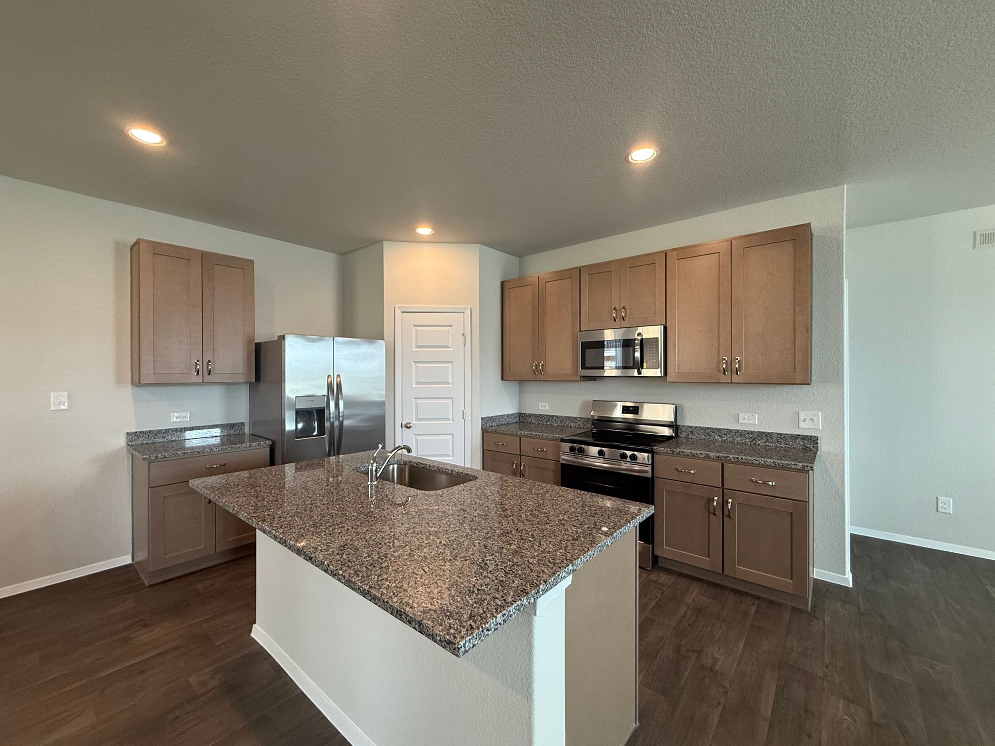 Kitchen with appliances with stainless steel finishes, dark wood-type flooring, dark stone countertops, an island with sink, and recessed lighting