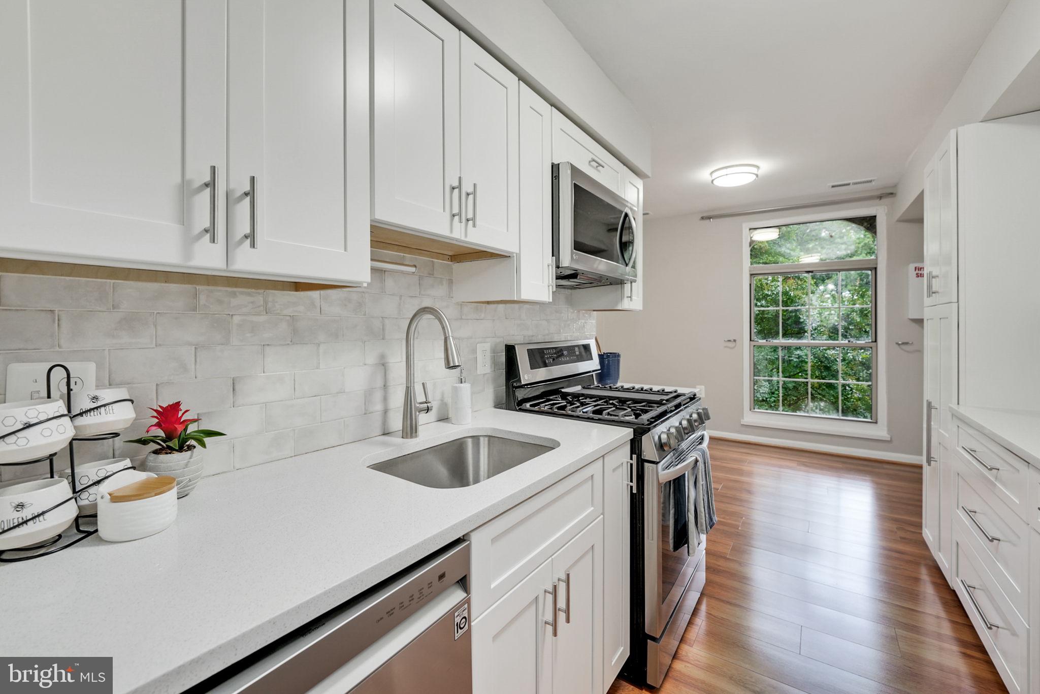 a kitchen with stainless steel appliances granite countertop a sink stove and white cabinets with wooden floor