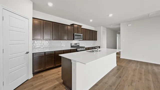 a kitchen with stainless steel appliances a sink a stove top oven a refrigerator with wooden floors