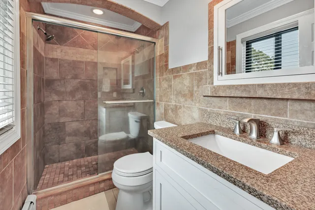 a bathroom with a granite countertop sink a toilet a mirror and shower