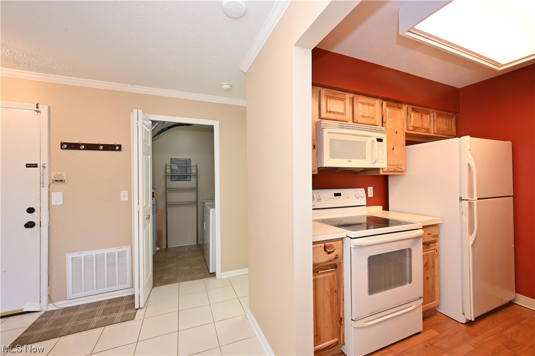 28140 Detroit Road, Unit A1 Westlake, OH 44145 - Photo 7 of 30 Kitchen featuring washer / clothes dryer, white appliances, light hardwood floors, and ornamental molding
