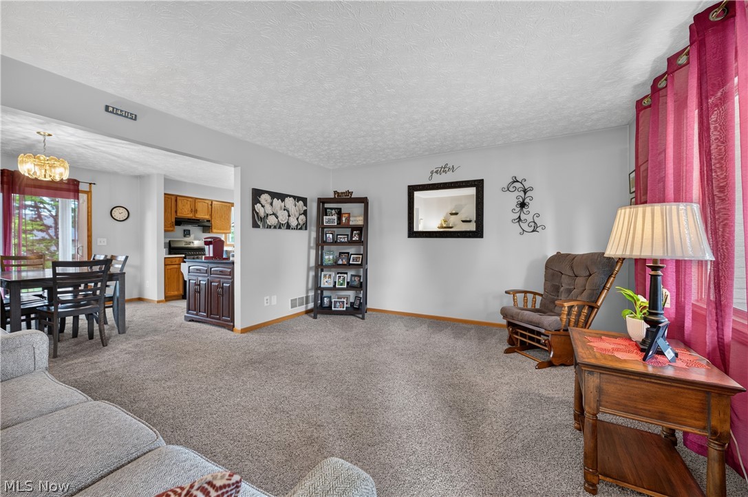763 Lockwood Road Barberton, OH 44203 - Photo 8 of 24 Carpeted living area with light gray walls, open entry to dining space with chandelier, and partial view of kitchen cabinetry