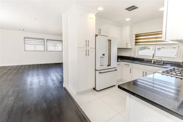 a kitchen with granite countertop a refrigerator a sink dishwasher a stove and white cabinets with wooden floor