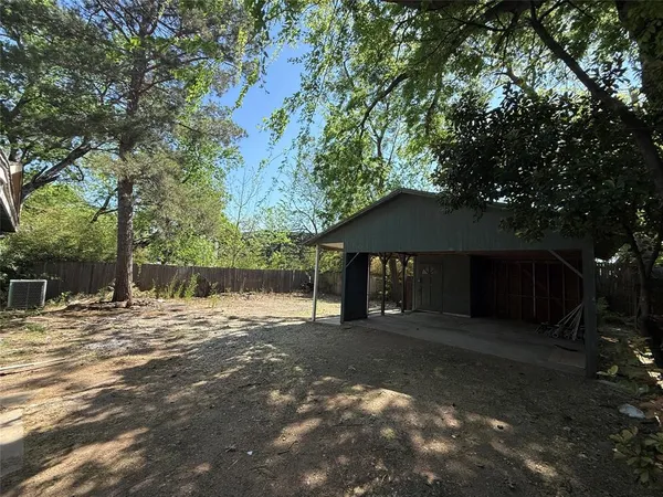 a backyard of a house with large trees and a wooden fence