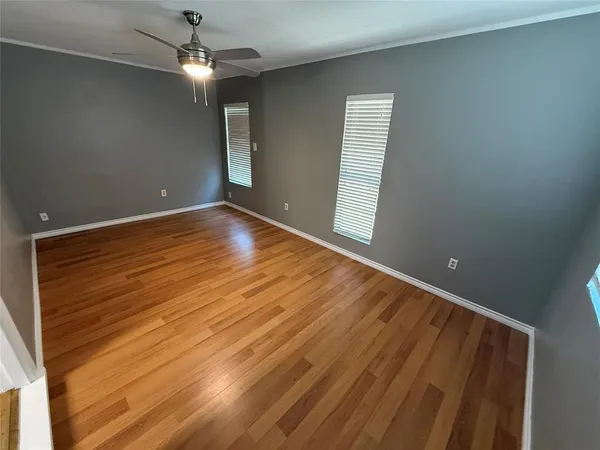 an empty room with wooden floor chandelier fan and windows