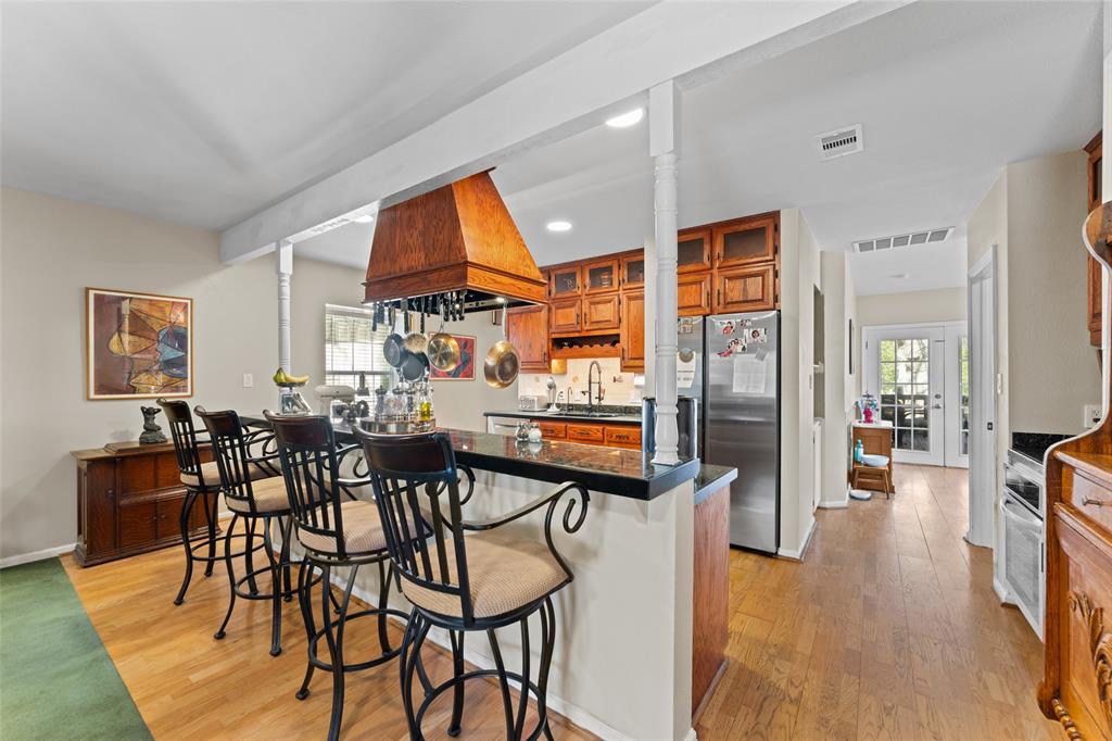 805 East Shady Grove Road Irving, TX 75060 - Photo 8 of 36 Kitchen with wood finish cabinetry, dark countertops, a breakfast bar, freestanding refrigerator, and light wood-type flooring