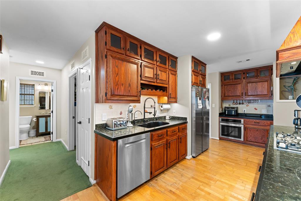 805 East Shady Grove Road Irving, TX 75060 - Photo 9 of 36 Kitchen featuring stainless steel appliances, wood finish cabinetry, glass fronted cabinets, light wood-style flooring, and recessed lighting