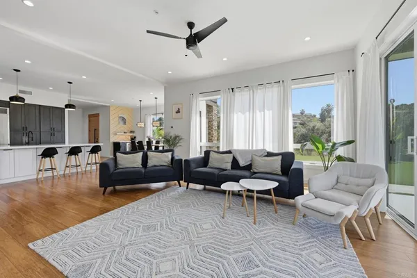 a large kitchen with stainless steel appliances granite countertop a stove a refrigerator a kitchen island a couches and a dining table with wooden floor