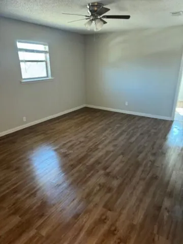 an empty room with wooden floor fan and windows