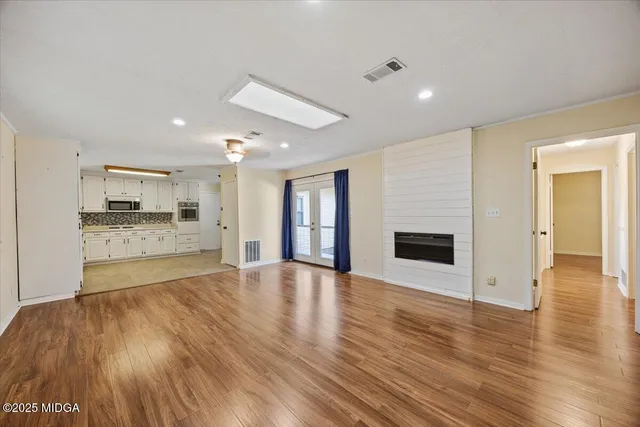 a view of an empty room with wooden floor and a kitchen