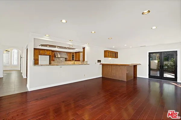 a view of an empty room with wooden floor and a kitchen