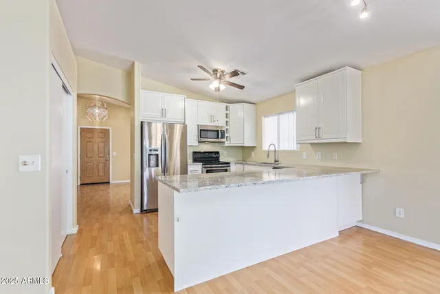 a large kitchen with stainless steel appliances a refrigerator a sink dishwasher a stove and white cabinets with wooden floor