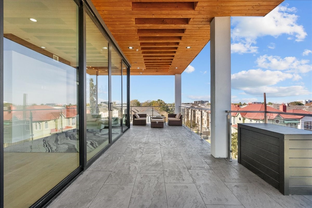 516 Reinerman Street Houston, TX 77007 - Photo 35 of 42 This photo showcases a spacious, modern balcony with sleek stone flooring and a wooden ceiling. It features comfortable outdoor seating, glass railings, and large sliding glass doors for seamless indoor-outdoor living, offering panoramic views of the surrounding neighborhood.