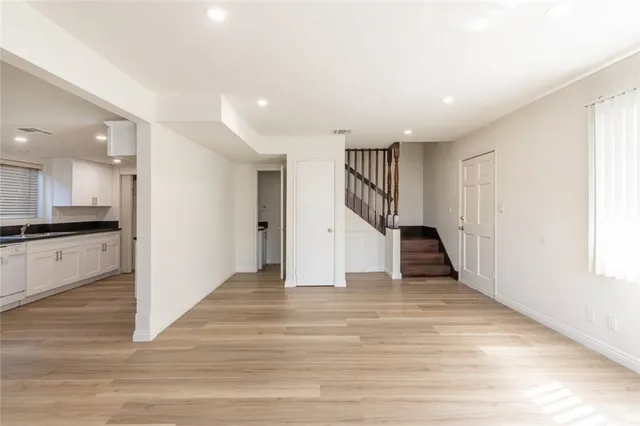 a view of an empty room with wooden floor and a kitchen