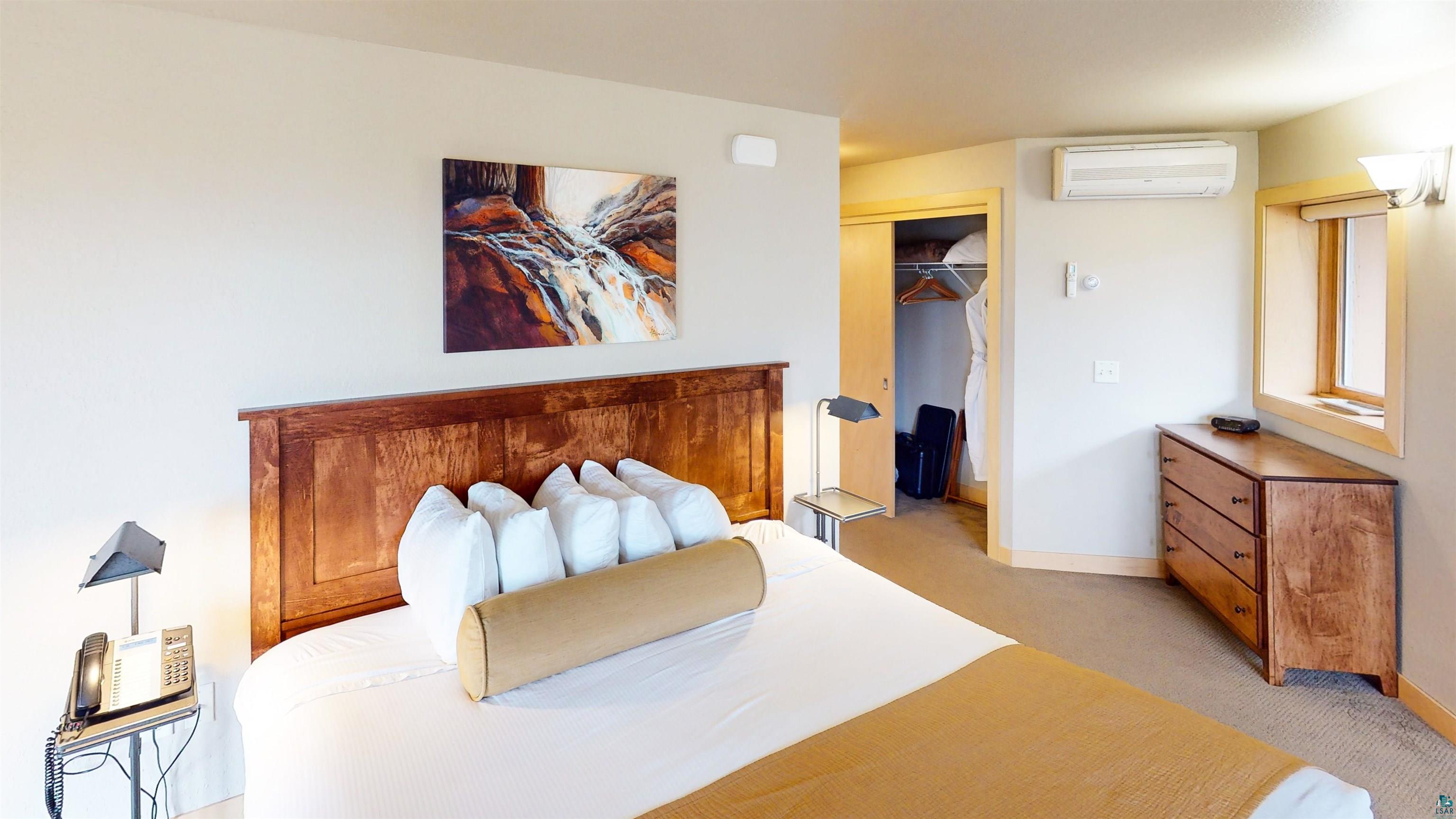 40 Surfside Drive, Unit 5D Tofte, MN 55615 - Photo 21 of 37 Spacious room featuring a wood-finish headboard, a built-in closet with sliding doors, a wall-mounted AC unit, a window with wood-finish trim, and a three-drawer wood-finish dresser