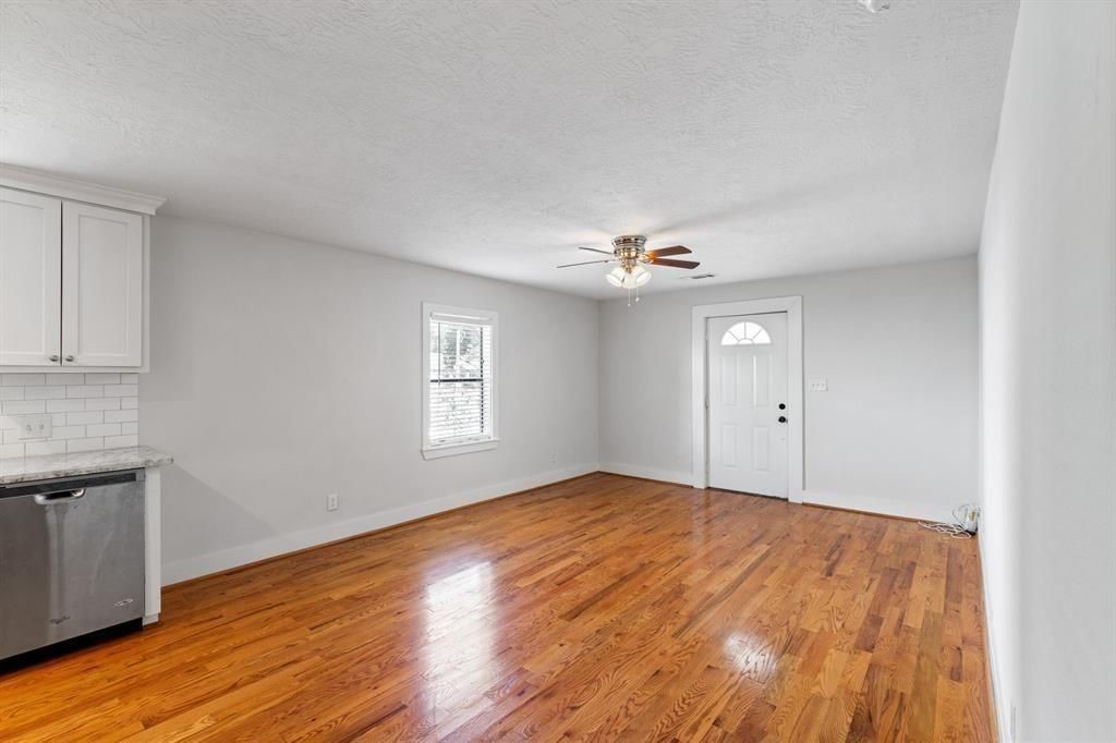 1305 Idylwild Street Houston, TX 77009 - Photo 8 of 31 This bright, open room features hardwood floors and a ceiling fan, with a small kitchen area including white cabinets and a stainless steel dishwasher. A window and entry door provide ample natural light.