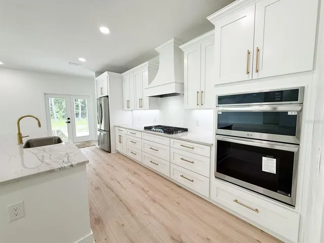 a kitchen with granite countertop a refrigerator stove and white cabinets with wooden floor