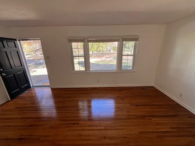 a view of an empty room with wooden floor and a window