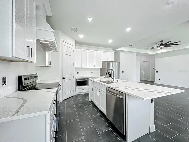 a view of kitchen with granite countertop stainless steel appliances stove a sink dishwasher a refrigerator and white cabinets with wooden floor