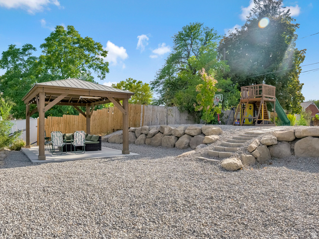 523 South Main Street Payson, UT 84651 - Photo 37 of 41 Gravel backyard featuring a wooden gazebo with a metal roof on a concrete pad, a rock retaining wall with integrated steps, and mature trees