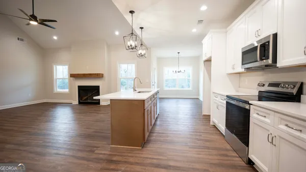 a large kitchen with stainless steel appliances granite countertop a stove top oven a refrigerator a sink and a wooden floor
