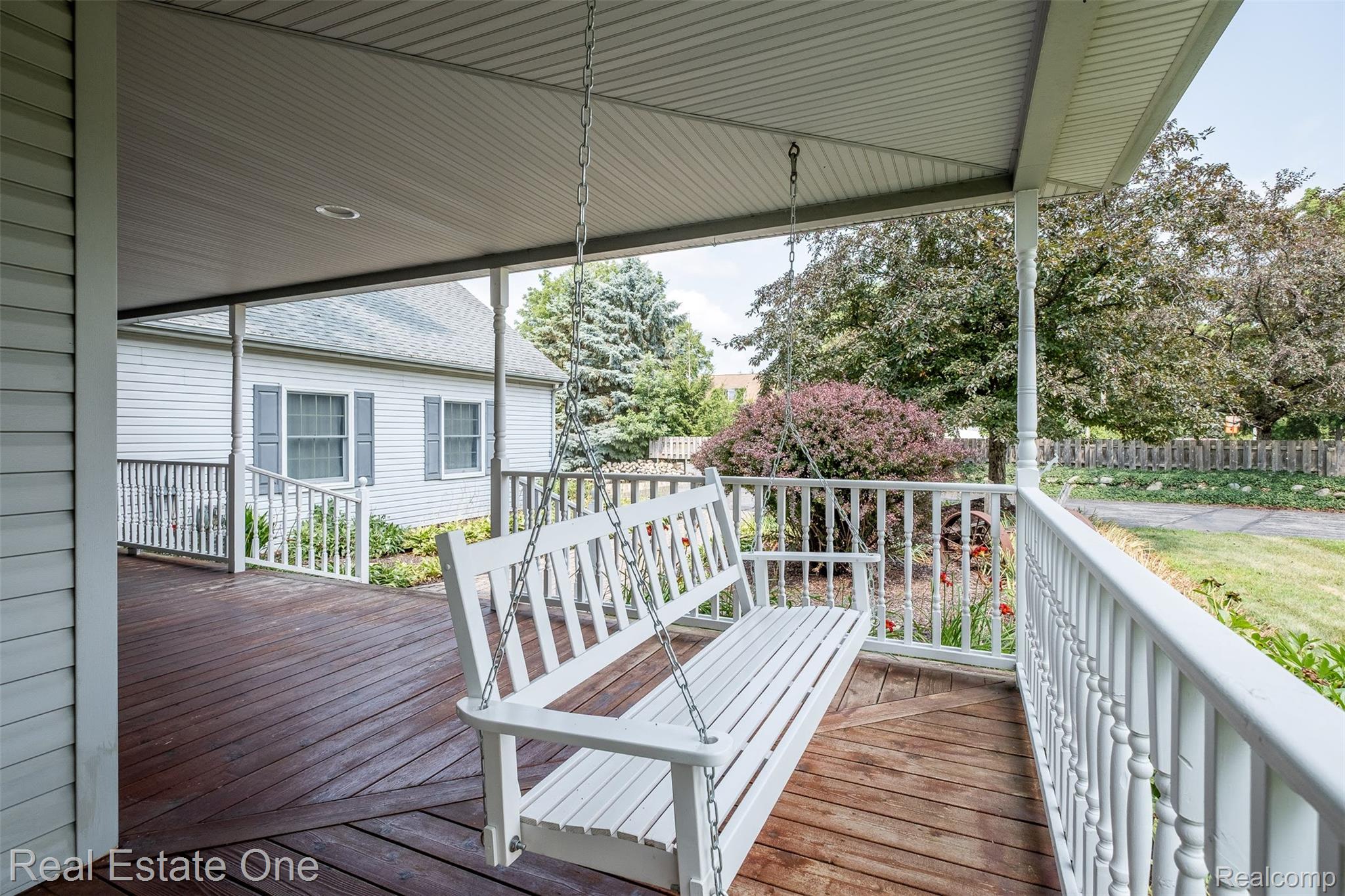 11030 Marshall Road South Lyon, MI 48178 - Photo 14 of 83 Covered wraparound porch featuring white balustrade railings, wood-finish decking, and a suspended swing