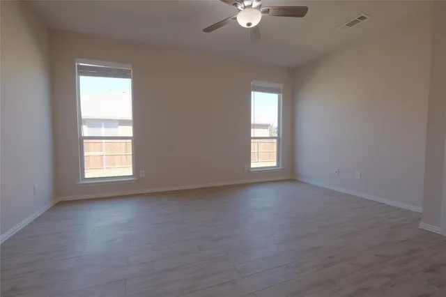 an empty room with wooden floor chandelier fan and windows