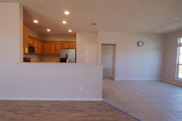 a view of an empty room with kitchen and window