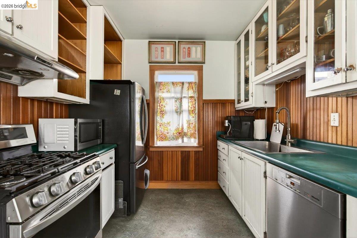 1013 Addison Street Berkeley, CA 94710 - Photo 22 of 57 Kitchen with stainless steel appliances, white cabinetry, wooden walls, glass fronted cabinets, and concrete floors