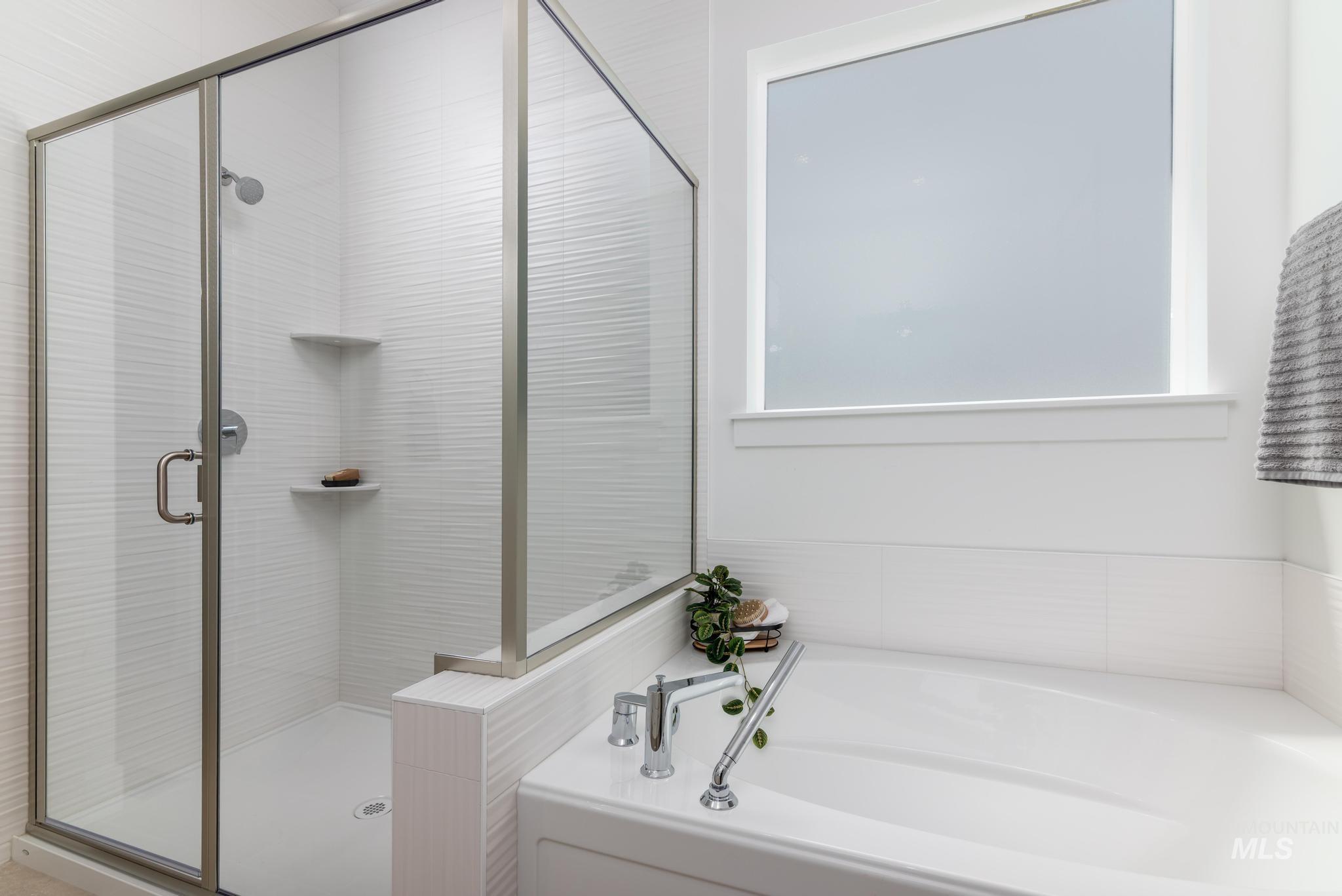8501 South Country Wind Avenue Meridian, ID 83642 - Photo 20 of 39 Shower and tub combination featuring a clear glass enclosure with brushed metal framing, white textured tile, built-in corner shelves, and a white soaking tub