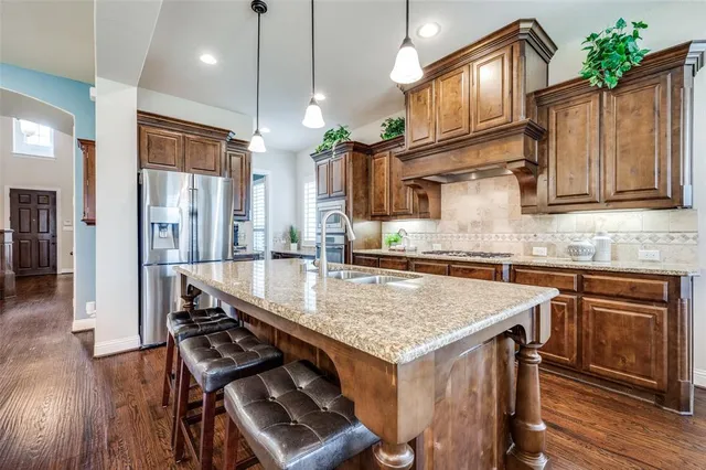 a kitchen with stainless steel appliances granite countertop a stove a sink dishwasher and a refrigerator with wooden floor