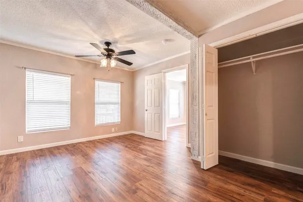 an empty room with wooden floor chandelier fan and windows