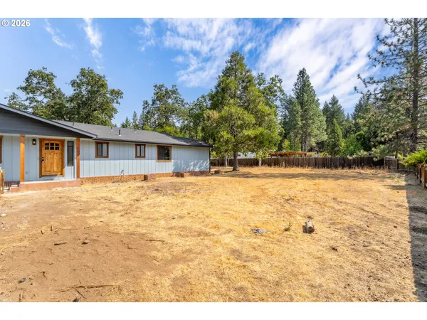 a backyard of a house with large trees and wooden fence