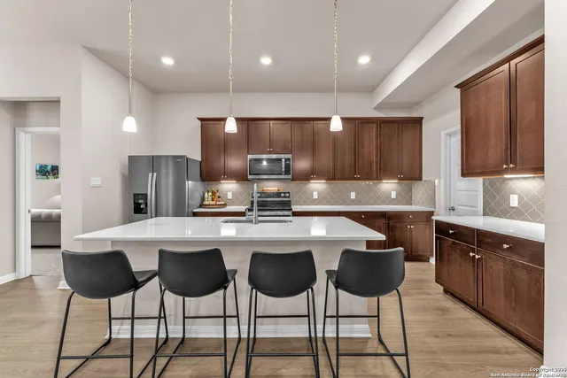 a kitchen with stainless steel appliances granite countertop a stove a refrigerator a sink and white cabinets with wooden chairs