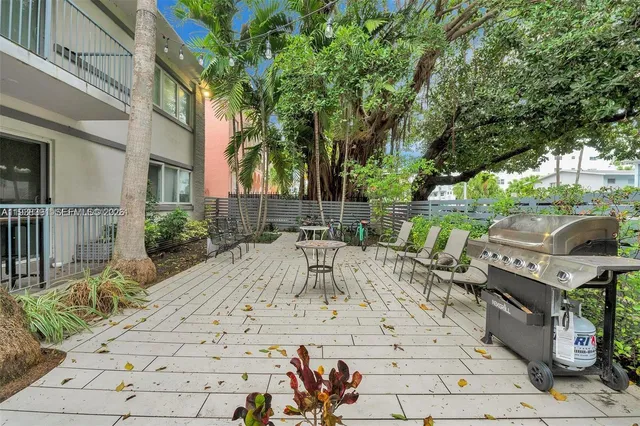 a view of a patio with table and chairs under an umbrella with large trees