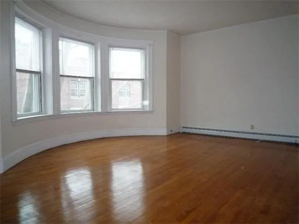 an empty room with wooden floor and windows with curtains